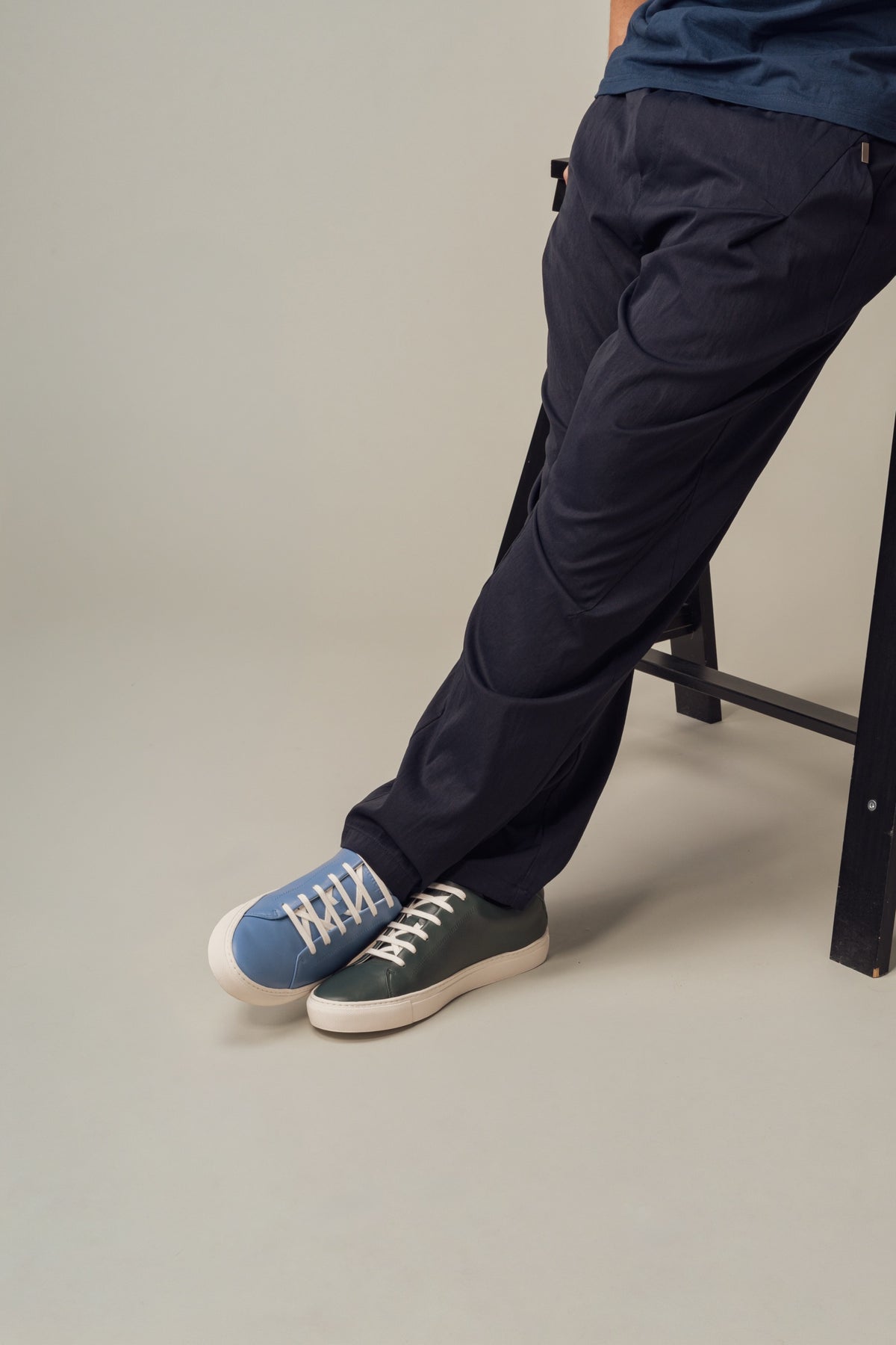 Feet in one light blue and one dark green sneaker beside a black stool
