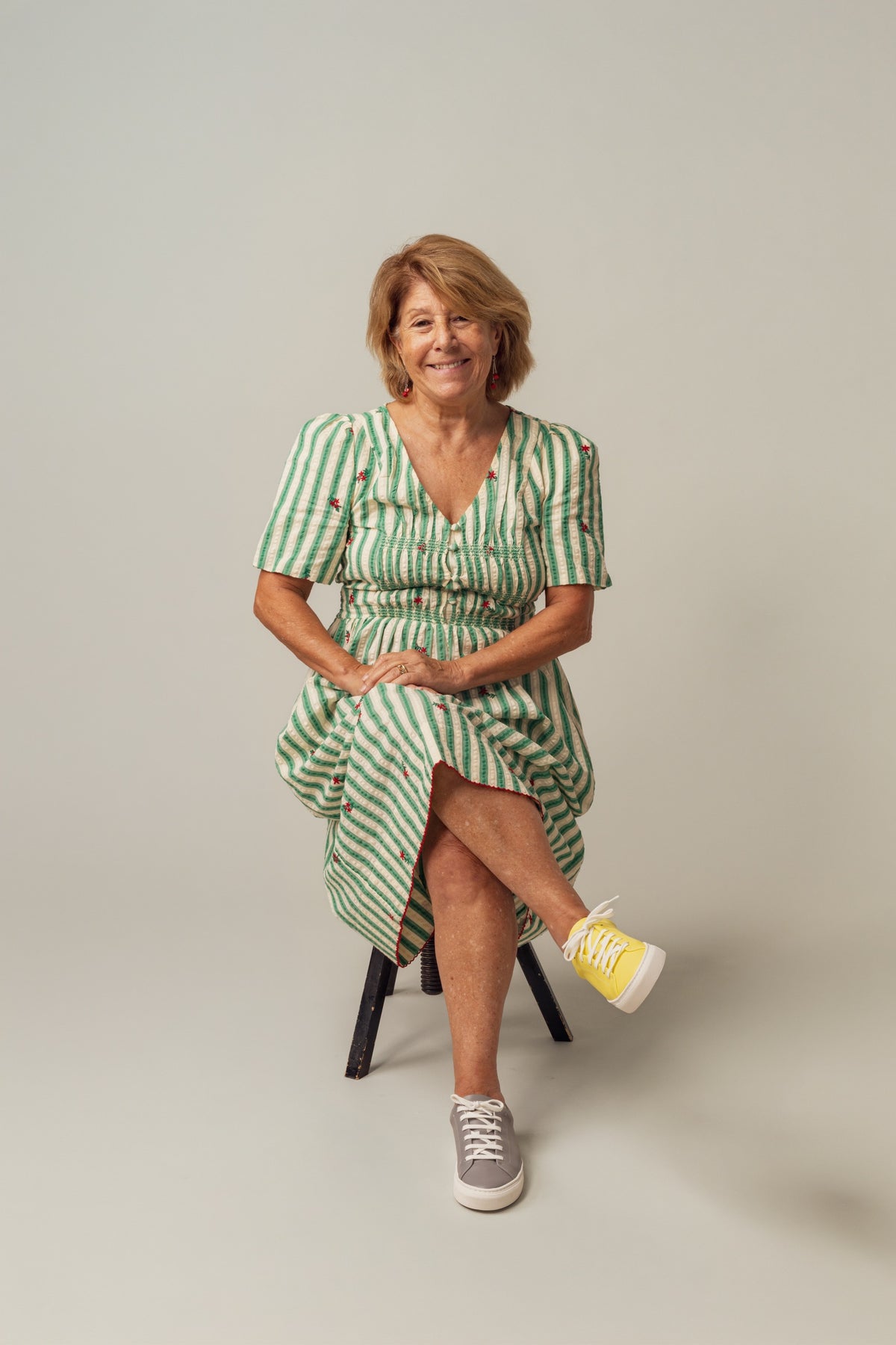 A smiling woman in a green striped dress wearing one yellow and one grey sneaker