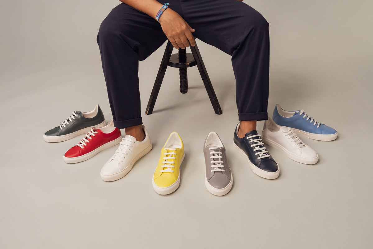 A man seated on a stool with the eight Unique x JAK sneakers arranged in an arc at his feet