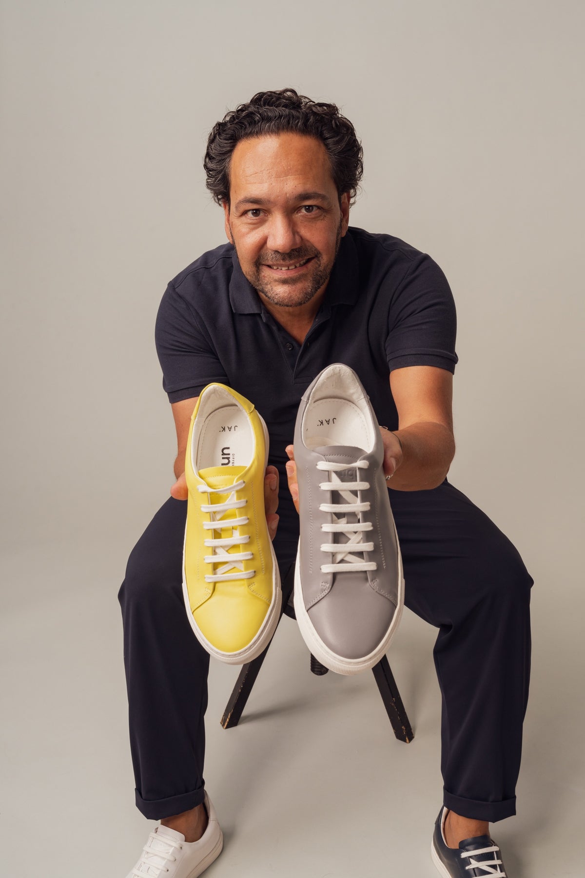 A smiling man holding out one yellow and one grey sneaker